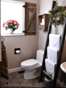 Wooden ladder in a bathroom with folded towels hanging from it.