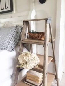 Wooden ladder acting as a nightstand next to a bed.