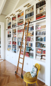 Giant wall covered in bookshelves with a tall ladder on wheels.