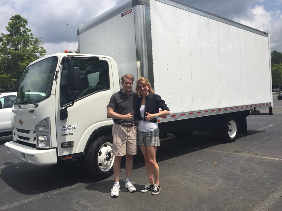 Man and woman posing in front of home staging moving truck