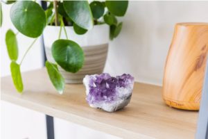 Crystal on a floating shelf next to an oil diffuser and house plant.